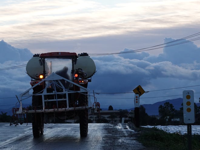 A man drives a farm vehicle past hoop houses, at right, in Camarillo early Saturday as clouds hang in the distance.