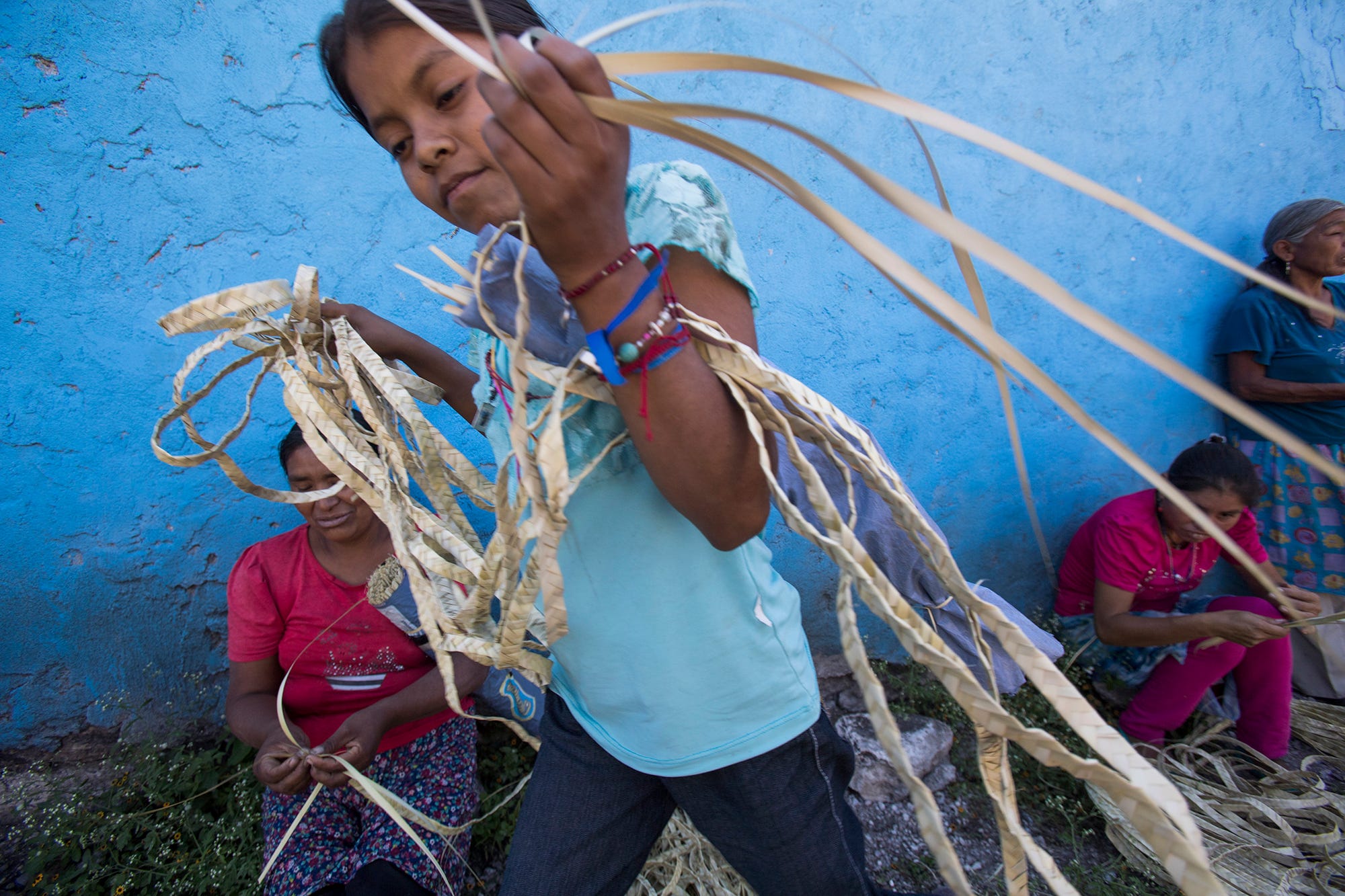 A child carries thin strips of dried palm leaves, which they sell at craft markets. Buyers weave them into hats and baskets.