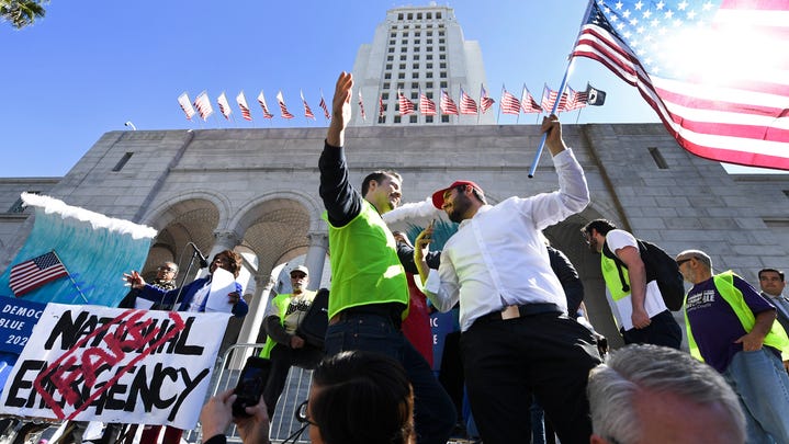 A Trump supporter holding an American flag confronts a security guard during a Los Angeles protest against President Trump's declaration of emergency to build a border wall.