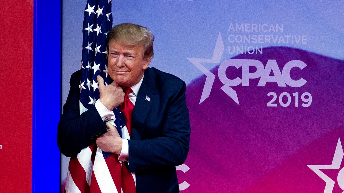 President Donald Trump hugs the American flag as he arrives to speak at Conservative Political Action Conference, CPAC 2019, in Oxon Hill, Md., on Saturday.