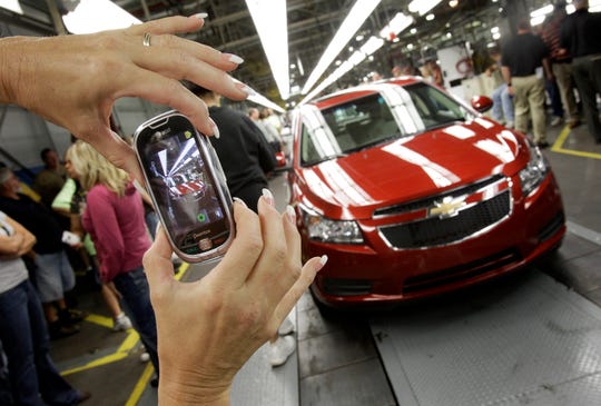 REPORT - In this photo from September 8, 2010, a car worker takes a picture of the first compact Chevrolet Cruze hatchback off the assembly line at a ceremony inside the GM plant in Lordstown, Ohio . GM employees in Lordstown and other factories in Michigan and Maryland that are expected to close within a year say the move will force them to leave behind parents or even their children in some cases.