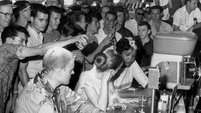 A mob opposed the demonstrators at a sit-in at Woolworth's lunch counter in Jacksonson, Miss., on May 28, 1963. A man is pouring sugar over the head of Joan Trumpauer Mulholland. Seated to her left is Anne Moody and to her right is John Salter Jr. Of the three, Mulholland is the only one still living.