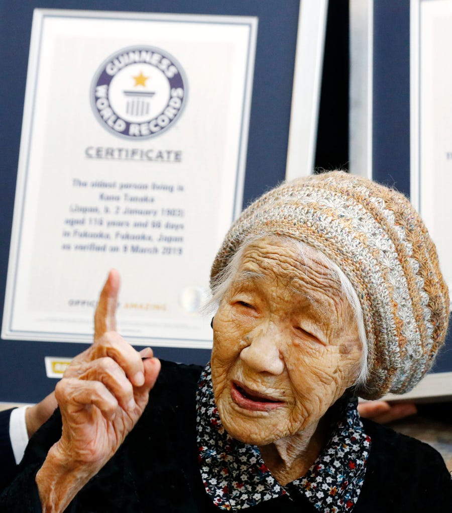 Kane Tanaka, a 116-year-old Japanese woman, gestures after receiving a Guinness World Records certificate, back, at a nursing home where she lives in Fukuoka, Japan on Saturday, March 9, 2019. 