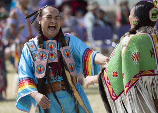 John Sneezy of the San Carlos Apache tribe dances at the Native Two Spirit Powwow  native american LGBT man laughing and wearing traditional ceremonial outfit colored blue with rainbows