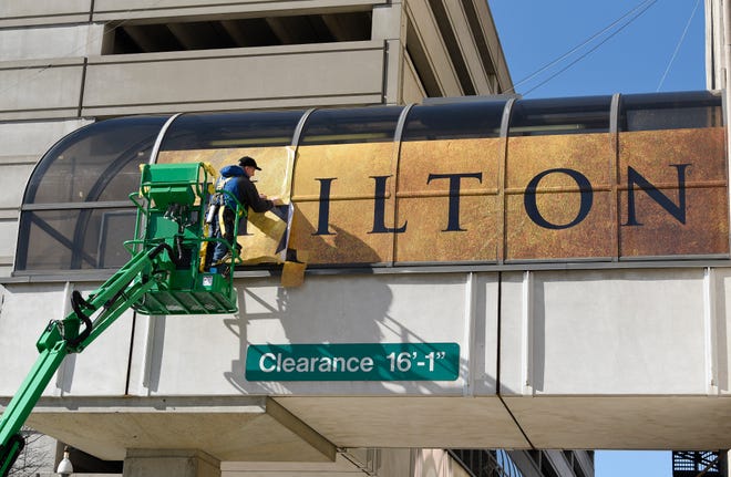 Ronald Justice, installer for Faro Imaging in Canton, installs a 'Hamilton' banner on the west side skywalk connecting to the Fisher Theatre Monday afternoon.