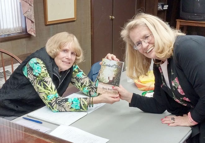 Judi Brett (right), who writes under the name Reece Brett, presents a copy of her book to Ann Starkey during a meeting of the Woman’s Club of Vineland.
