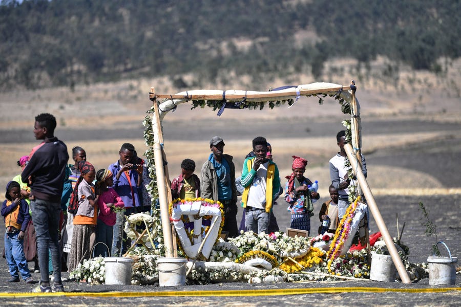 Children from surrounding homesteads stand in front of a flower memorial held for victims at the crash site of an Ethiopian airways operated by a Boeing 737 MAX aircraft on March 16, 2019 at Hama Quntushele village near Bishoftu in Oromia region. The second crash involving the 737 MAX series has spurred reaction among international airline operators to ground Boeing 737 Max aircraft in their fleets. 