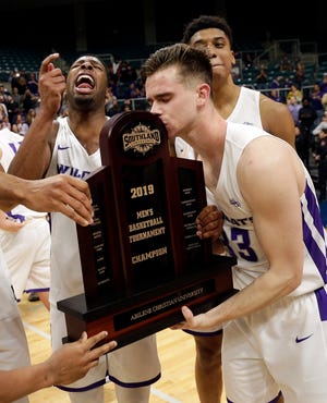 Abilene Christian guard Jaylen Franklin, left, yells as guard Paul Hiepler (33) kisses the championship trophy after the team's win Saturday over New Orleans for the Southland Conference men's tournament title.