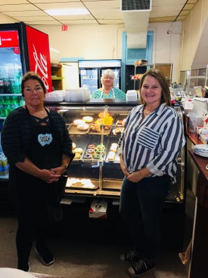 Patty Cakes Village Bake Shop owners Nancy Calvert and Kelly Burnworth stand in front of a display of baked items while cake decorator Lisa White stands in the background