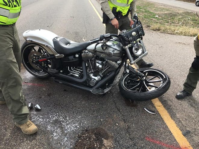 A San Juan County Sheriff's Office deputy holds a motorcycle involved in a collision with a silver car Tuesday on New Mexico Highway 516 near Flora Vista.