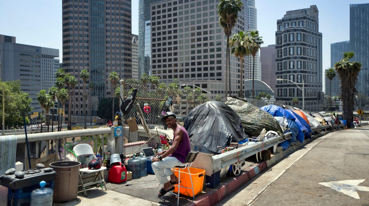 A homeless man sits at his tent along the Interstate 110 freeway in downtown Los Angeles. California Gov. Gavin Newsom met with the mayors of some of California's largest cities to discuss the homeless situation last month.