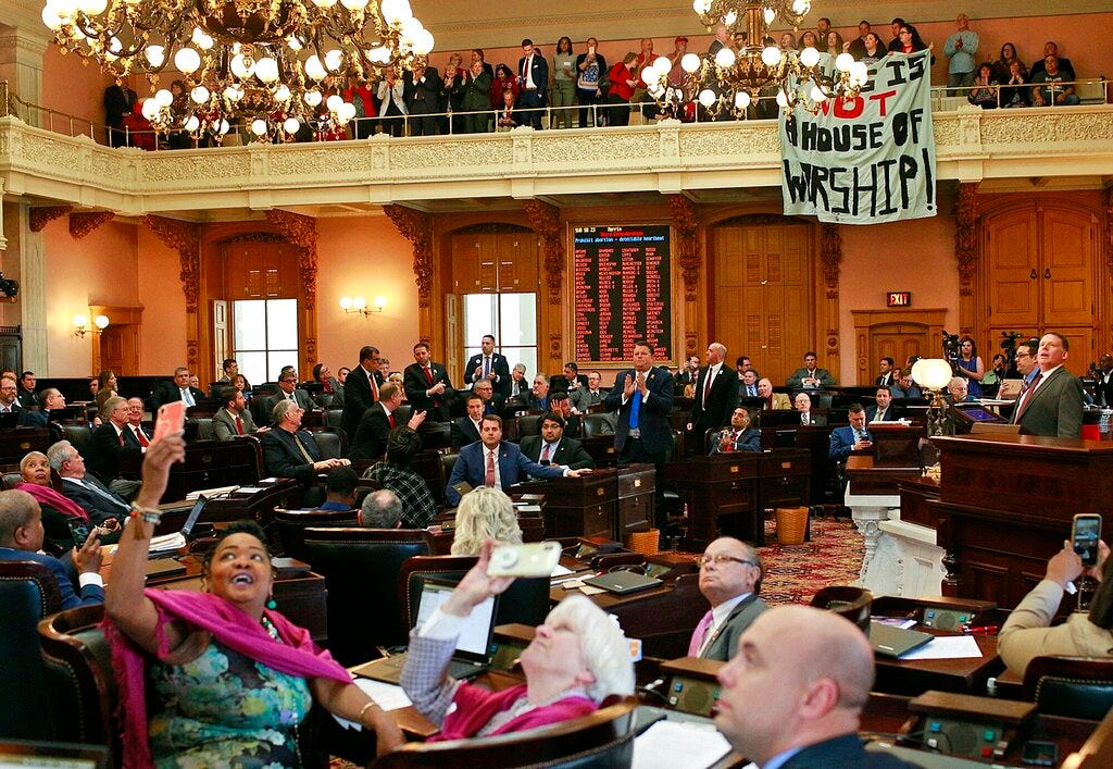 Some members of the Ohio House applaud following their April 10, 2019, vote on the state's "heartbeat" bill. Others photograph protesters who unfurled banners reading "This is not a House of Worship" and "This is not a Doctor's office."