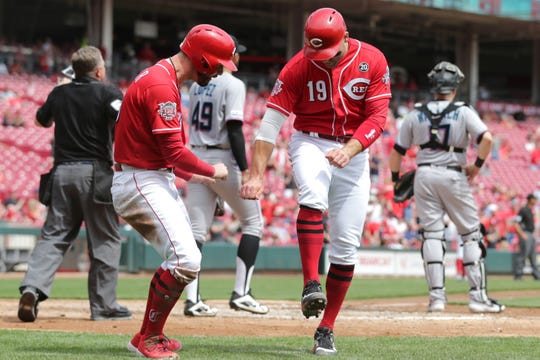Cincinnati Reds right fielder Jesse Winker (33), left, and Cincinnati Reds first baseman Joey Votto (19), right, celebrate scoring on a double by Cincinnati Reds right fielder Yasiel Puig (66) in the fifth inning of an MLB baseball game against the Miami Marlins, Thursday, April 11, 2019, at Great American Ball Park in Cincinnati. 
