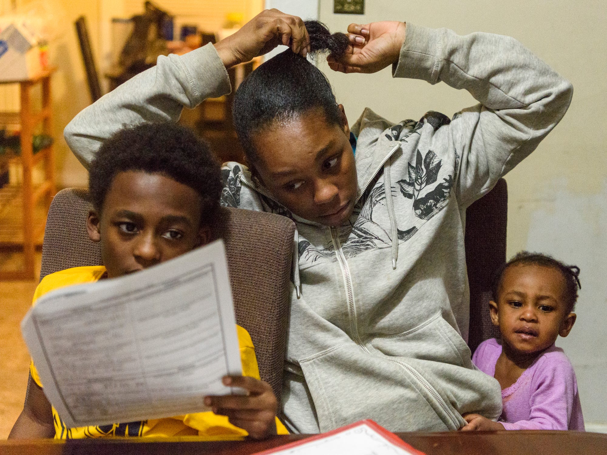 Tamisha Dilworth, center, looks over her son Travon's homework as her daughter Teresa vies for her attention, Wednesday evening, Feb. 13, 2019. Dilworth works long hours every weekend as a Certified Nursing Assistant, which allows her to help her children get to and from school, do their homework and spend time together as a family on weekdays. 
