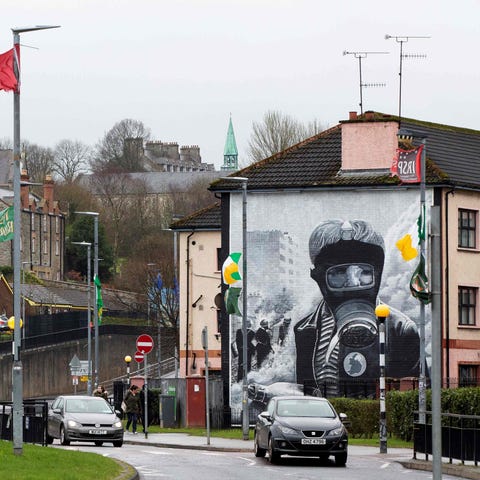 Cars pass murals in Derry, Northern Ireland, on...