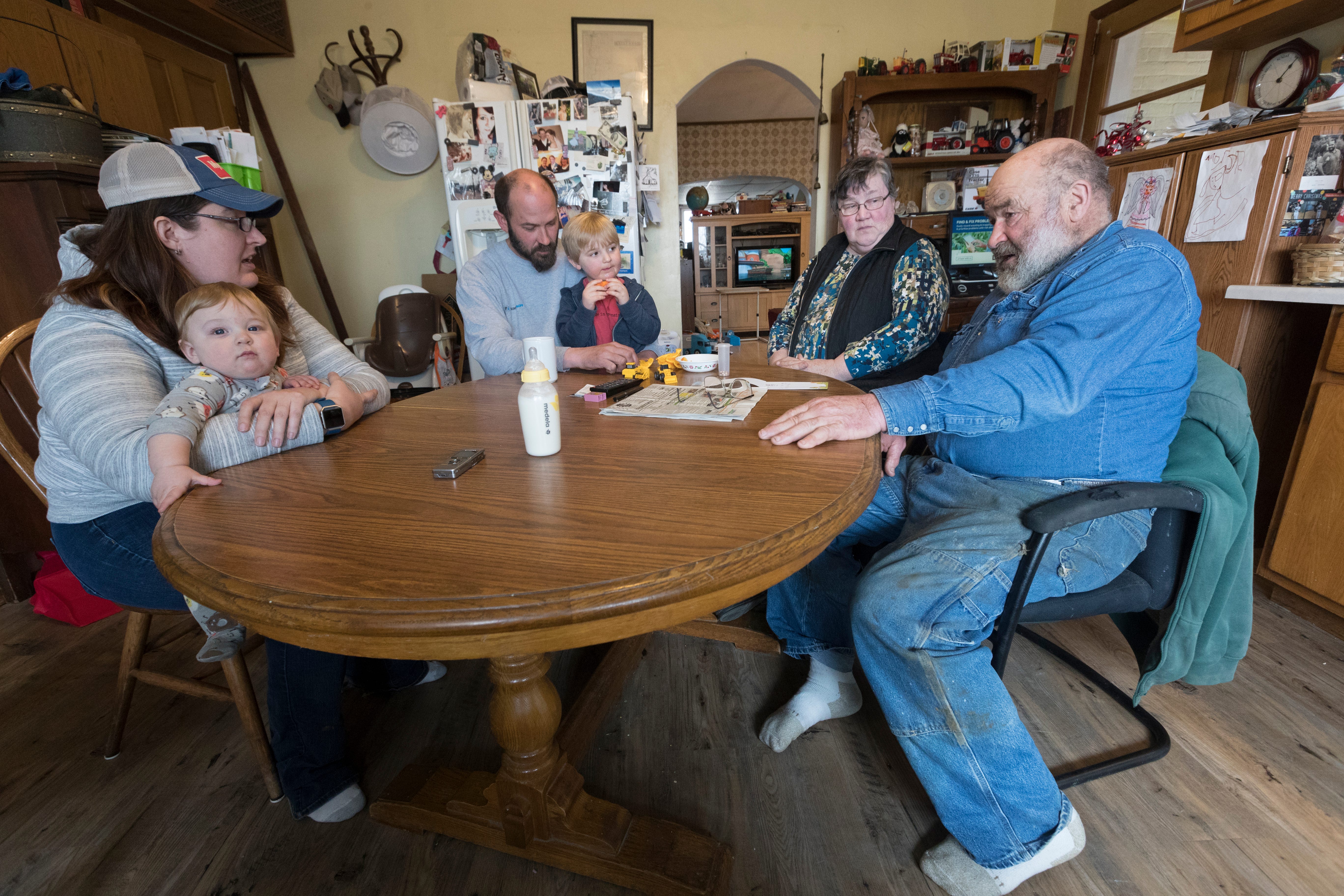 The Mess family, Carrie Mess, from left, with her 10-month-old son, Ben; husband, Patrick, with 3-year-old son Silas; and Cathy and Clem Mess, gather around their kitchen table on their farm in Watertown.