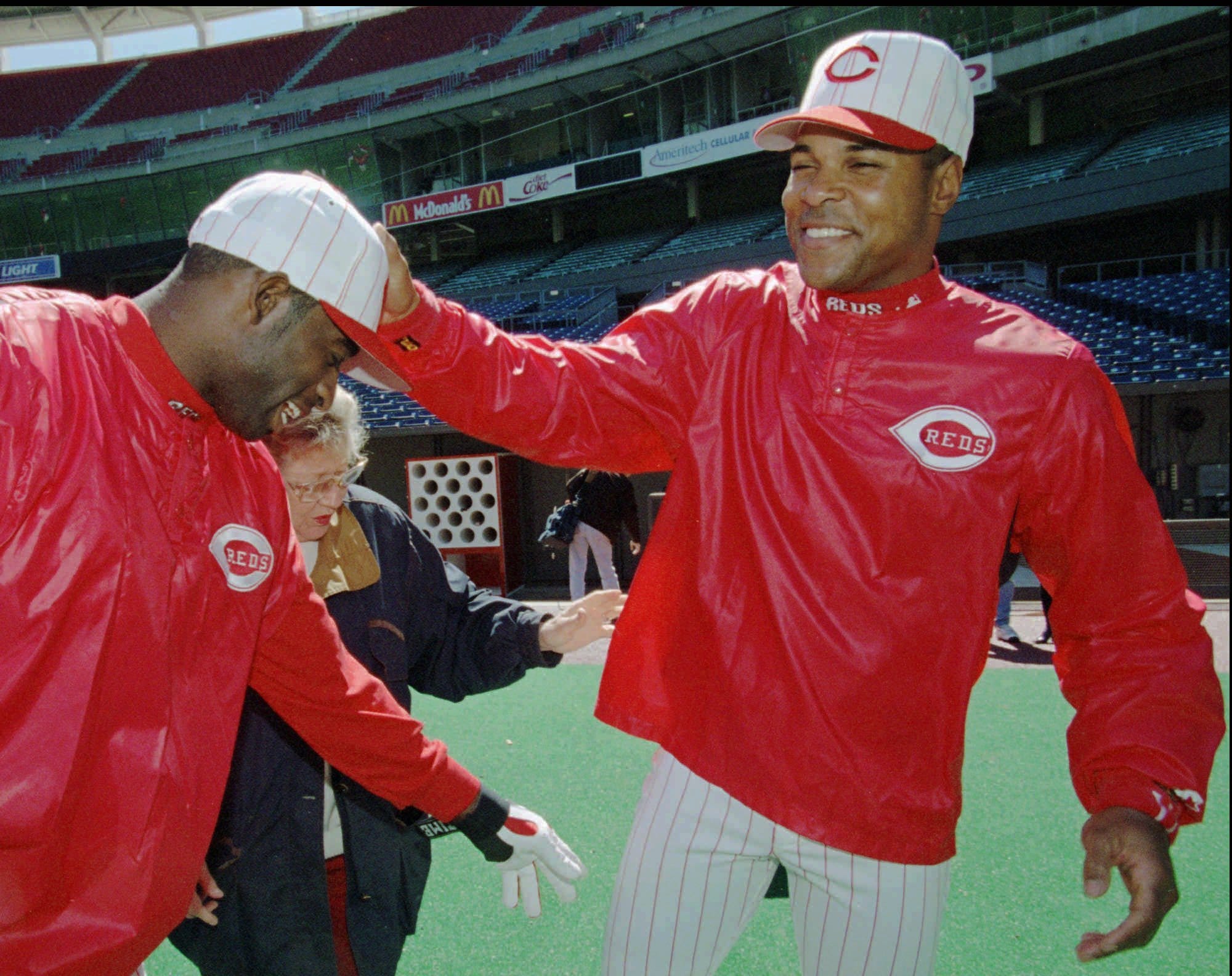 Text: Cincinnati Reds shortstop Barry Larkin, right, slaps Deion Sanders on the head as Sanders jokes with Larkin and Reds owner Marge Schott, center, during practice Monday, March 31, 1997, in Cincinnati. The Reds open against the Colorado Rockies Tuesday afternoon. (AP Photo/Al Behrman)