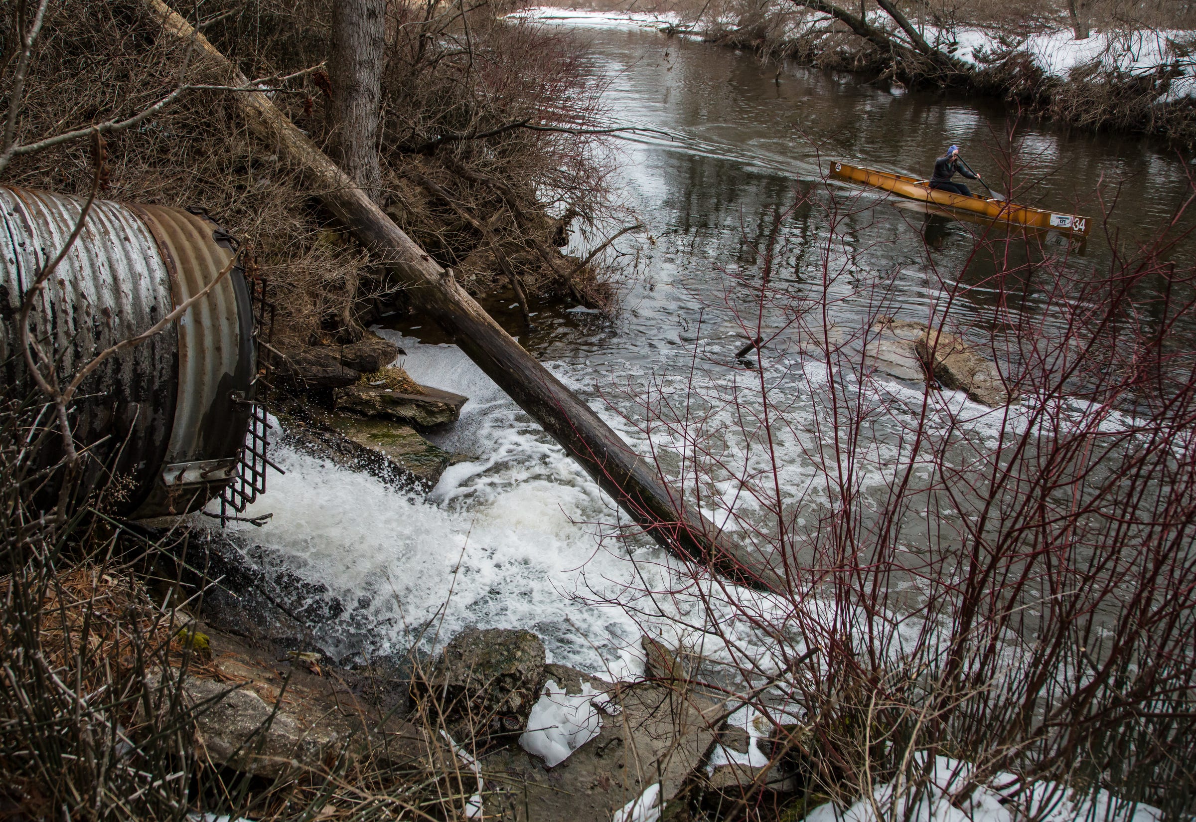 A person canoe's along Van Etten Creek in Oscoda Township on Wednesday, March 13, 2019 as a storm pipe pumps water treated at a granular activated carbon (GAC) plant from the former Wurtsmith Air Force Base into the lake leaving some PFAS foam to gather along the water. 