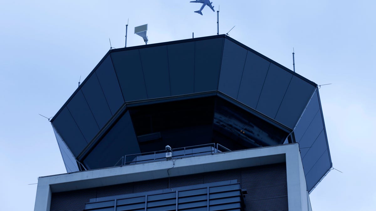 A plane flies over the south air traffic control tower at O'Hare International Airport Monday, April 22, 2019, in Chicago. The south control tower has been awarded gold status by a group that monitors standards for eco-friendly buildings. The tower is one of three that the FAA operates at O'Hare. (AP Photo/Kiichiro Sato)