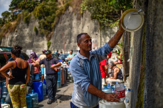 A man fills containers with water flowing down from the Wuaraira Repano mountain, also called "El Avila", in Caracas on March 13, 2019. The nationwide blackout in Venezuela has left millions without running water. Many people lined up to buy bottled water in Caracas supermarkets, but most are reduced to desperate means -- besieging fountains in public parks and any available water sources around the capital.