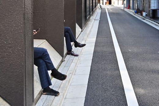 Businessmen check their phones as they have a break in Tokyo's Ginza district on April 3, 2019.