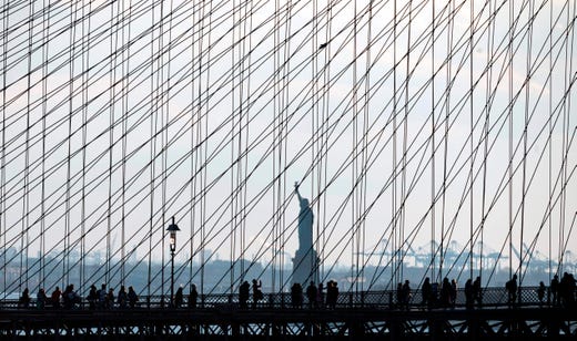 People walk on the Brooklyn Bridge in front of the Statue of Liberty on April 6, 2019 in New York City.