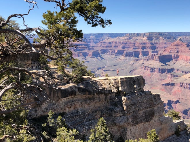 A visitor poses for a photo on a ledge off the Grand Canyon's South Rim.
