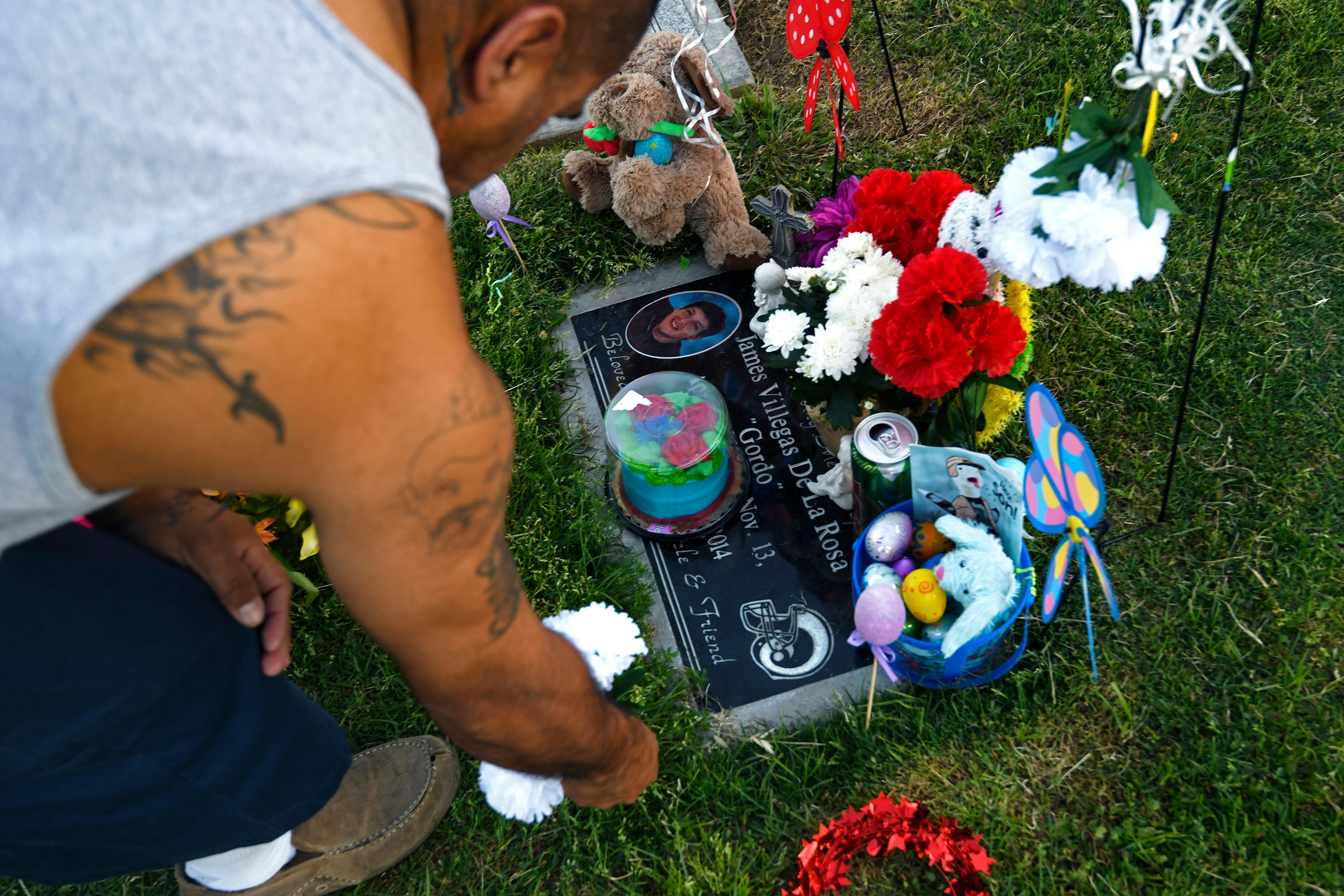 Eric Marmolejo places white flowers next to the headstone of his cousin, James de la Rosa.