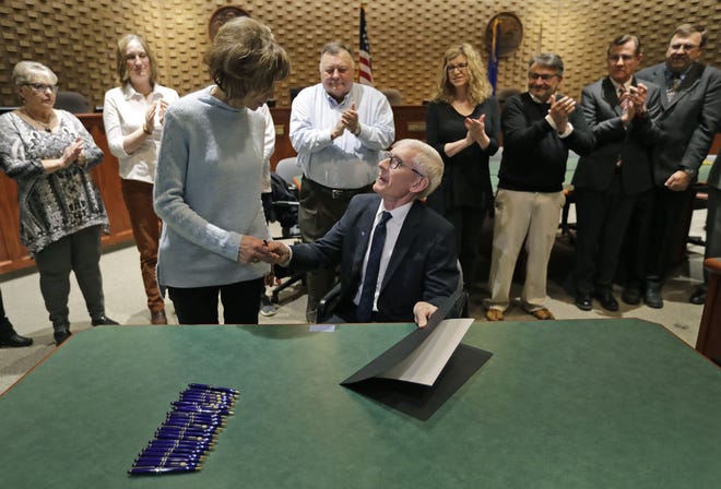 Gov. Tony Evers shares a moment with Sandy Ellis after he signed a bill naming the Interstate 41-U.S.10/State 441 interchange after the late state legislator Mike Ellis at Neenah City Hall. Sandy is the widow of Ellis. The two are surrounded by family, friends and officials.