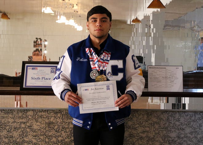 Fabian Padilla showcases his senior wrestling awards. On the left is his sixth-place finish at Virginia Beach. On his right is his State Championship bracket. He holds his All-American wrestler certificate and wears his three state wrestling medals around his neck.