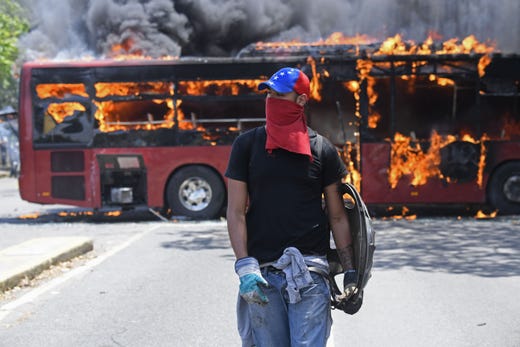 An opposition demonstrator walks near a bus in flames during clashes with soldiers loyal to Venezuelan President Nicolas Maduro after troops joined opposition leader Juan Guaido in his campaign to oust Maduro's government, in the surroundings of La Carlota military base in Caracas on April 30, 2019.