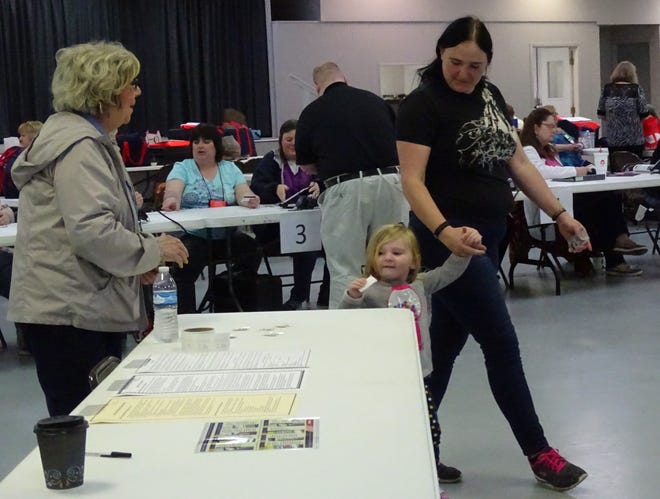 Elenore Sword, 3, and her mom, Sara Usher, hold hands as the two leave the polling place at the Crawford County Fairgrounds after Usher voted on Tuesday. Precinct worker Billie Wieland, left, was handing out stickers.