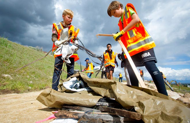 In a Wednesday, May 8, 2019 photo, Brenton Cramer, 10, left, and Damon Haub, 10, both of Lehi, gather trash into a pile as he and other volunteers help to complete an Eagle Scout Service Project that aims to create a walkable path connecting nearby neighborhoods to Ignite Entrepreneurship Academy and a future park, just northwest of the charter school in Lehi, Utah. (Isaac Hale/The Daily Herald via AP)