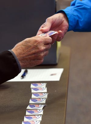 A poll worker gives an "I voted" sticker to a voter during the school board election Tuesday, May 21, in Sioux Falls.