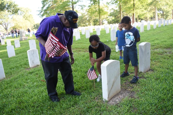 U.S. Army and Desert Storm veteran Christopher Josiah (far left) watches as granddaughter Ja'Nayah Lee places a flag at the headstone of one of the gravesites at the Alexandria National Cemetery Saturday, May 25, 2019. His grandsons Kayden Lee and Zaydin Lee also helped. are Volunteers placed flags on the 7,816 gravesites at the Alexandria National Cemetery in preparation for the Memorial Day program set for Monday. Alexandria mayor Jeff Hall is the guest speaker. The cemetery is located at 209 East Shamrock Street in Pineville. The Memorial Day program begins at 9:45 a.m. Monday. A patriotic musical and reading, placing of wreaths by various Veteran service organizations, a rifle salute and the playing of taps are among the program activities. All Americans are asked to participate in a National Moment of Remembrance at 3 p.m. Monday to remember and honor military personnel who died in service to the U.S.