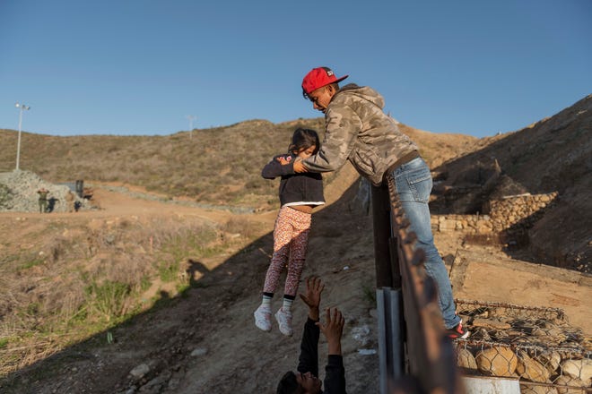 A migrant from Honduras passes a child to her father after he jumped the border wall to get into the U.S. side to San Diego, Calif., from Tijuana, Mexico, on Jan. 3.