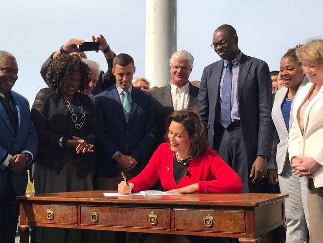 Michigan Gov. Gretchen Whitmer signs historic no-fault auto insurance reform legislation on May 30, 2019 as the Legislature's two Republican leaders look on.