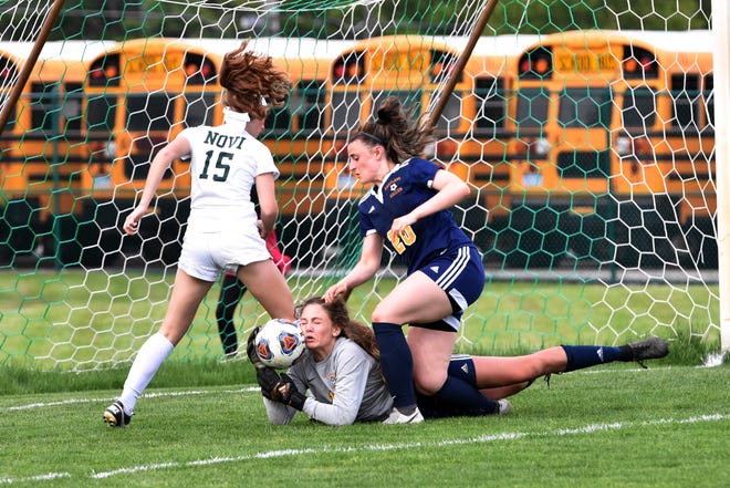 Hartland goalie Cassidy Vaughn makes a save while Novi's Avery Fenchel (15) and Hartland's Lauren Smith (20) converge on the ball in a district soccer semifinal on Wednesday, May 29, 2019.