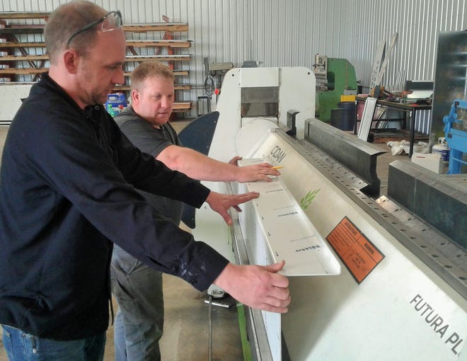 Owner Marcus Henning (left) and his employee Creighton Regenwether operate this computerized folding machine at Architectural Metal Folding in North Liberty. This panel will end up on a new Kansas City building.