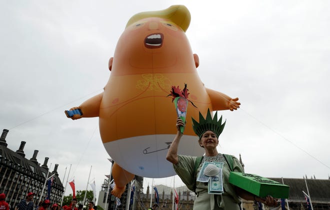A woman posing as the Statue of Liberty stands next to the 'Trump Baby' blimp as people gather to demonstrate against the state visit of President Donald Trump in Parliament Square, central London, Tuesday, June 4, 2019.
