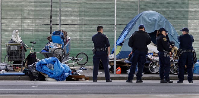 In this March 1, 2016, file photo, San Francisco police officers wait while homeless people collect their belongings in San Francisco. San Francisco supervisors are considering legislation Tuesday, June 4, 2019, allowing the city to force mentally ill drug addicts into housing and treatment for up to a year.