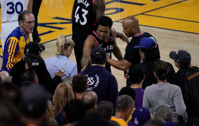 Toronto Raptors guard Kyle Lowry, middle, gestures next to referee Marc Davis (8) near the front row of fans during the second half of Game 3. A minority team owner seated courtside  was ejected after shoving Lowry when the Raptors star crashed into a row of seats while trying to save a ball from going out of bounds on Wednesday night.