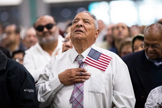 A new U.S. citizen holds an American flag as he sings the national anthem during a naturalization ceremony at a convention center in Los Angeles, Calif, May 22, 2019. 
