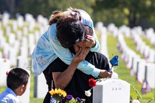 Cesar Martinez cries as he kneels at the grave of his brother Rodrigo, who died in Iraq in 2004, while being held by his cousin Carla on Memorial Day at the Los Angeles National Cemetery in Los Angeles, Calif., May 27, 2019.