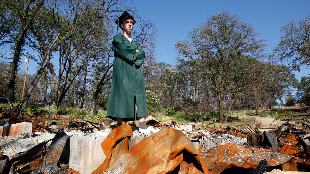 In this June 5, 2019, photo, Sean Newsom, a senior at Paradise High School, poses in his cap and gown at the burned out ruins of his home in Paradise, Calif. The Northern California town that was mostly destroyed by a wildfire is celebrating high school graduation.