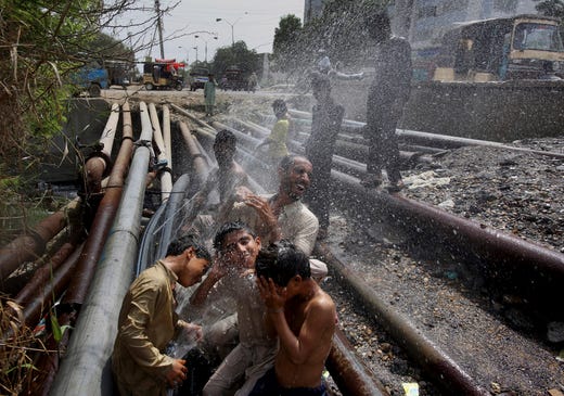 People cool themselves off in spray from broken water pipes at a road side in Karachi, Pakistan, where temperature reached above 42 degrees Celsius (108 Fahrenheit), Thursday, June 13, 2019. The meteorological department Thursday issued an alert, warning fishermen to avoid fishing in the Arabian sea this week as the Cyclone Vayu could cause rough conditions in the sea. (AP Photo/Fareed Khan) ORG XMIT: ISL104