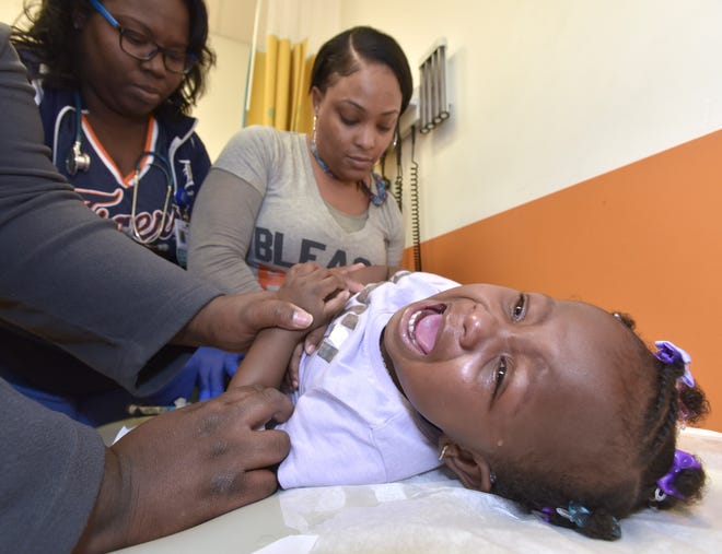 Fifteen-month-old Tavayah Noble of Detroit gets a vaccination from medical office assistants Cheri Lynch, left, and Lanesha Abram, right, while her mother, Kierra Hardwick, holds the toddler's hand.