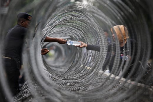 epaselect epa07647268 An Indonesian police officer buys a bottle of water through razor wire as he stands guard outside the Constitutional Court in Jakarta, Indonesia, 14 June 2019. Indonesia's authorities tightened security as trial hearings started in court to challenge the results of the presidential election. EPA-EFE/MAST IRHAM ORG XMIT: MAS301