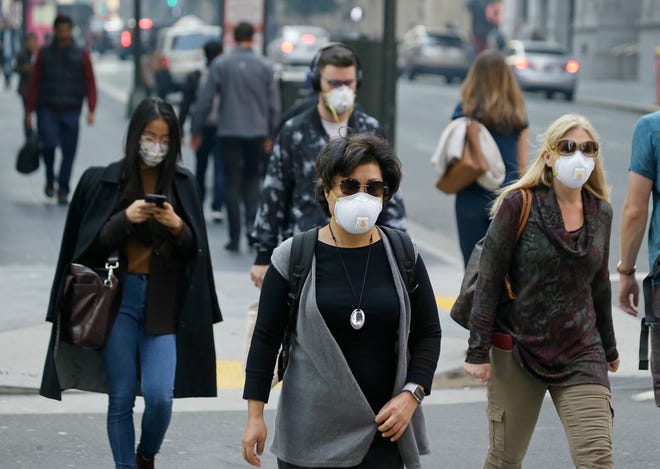 In this Friday, Nov. 9, 2018 file photo, people wear masks while walking through the Financial District in the smoke-filled air in San Francisco, as authorities issued an unhealthy air quality alert for parts of the San Francisco Bay Area as smoke from a massive wildfire drifts south.
