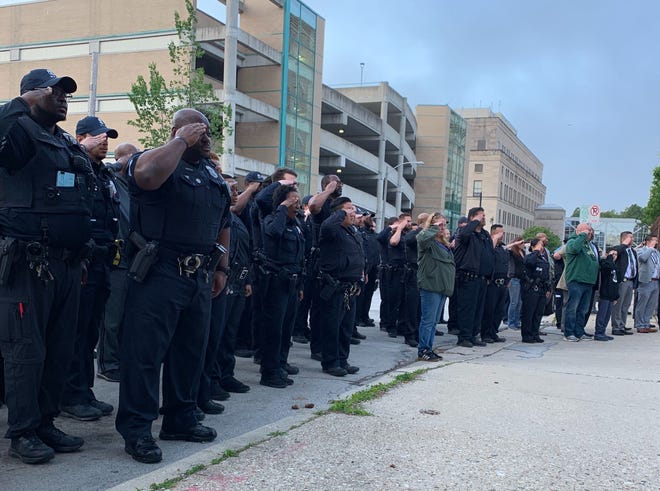Officers salute as the body of  Milwaukee Police Officer Kou Her arrives at the Milwaukee County Medical Examiner's Office Tuesday morning. The off-duty officer was killed in an overnight car crash.